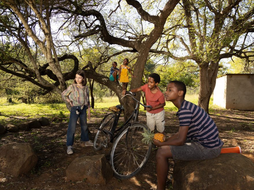 Die Kinder aus dem Film Thabo - das Nashorn Abenteuer stehen und sitzen zwischen Bäumen und blicken nach links.