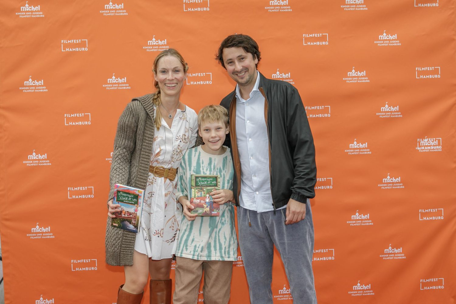 Auf dem Foto sind die Autorin Sabrina Kirschner, der Regisseur Ekrem Ergün und der junge Schauspieler Lucas Herzog zu sehen. Im Hintergrund sieht man die Logos vom MICHEL Kinder und Jugend Filmfest.